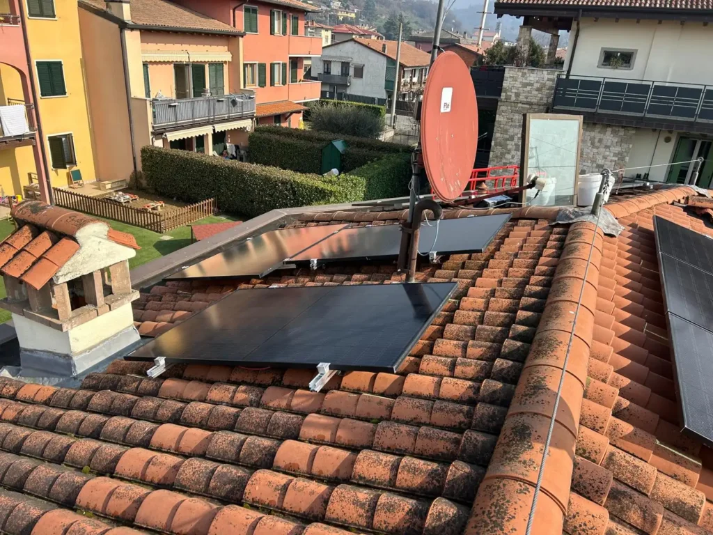 etto a tegole rosse con pannelli solari neri, un pannello riflettente chiaro e un'antenna parabolica rossa, in un contesto residenziale.