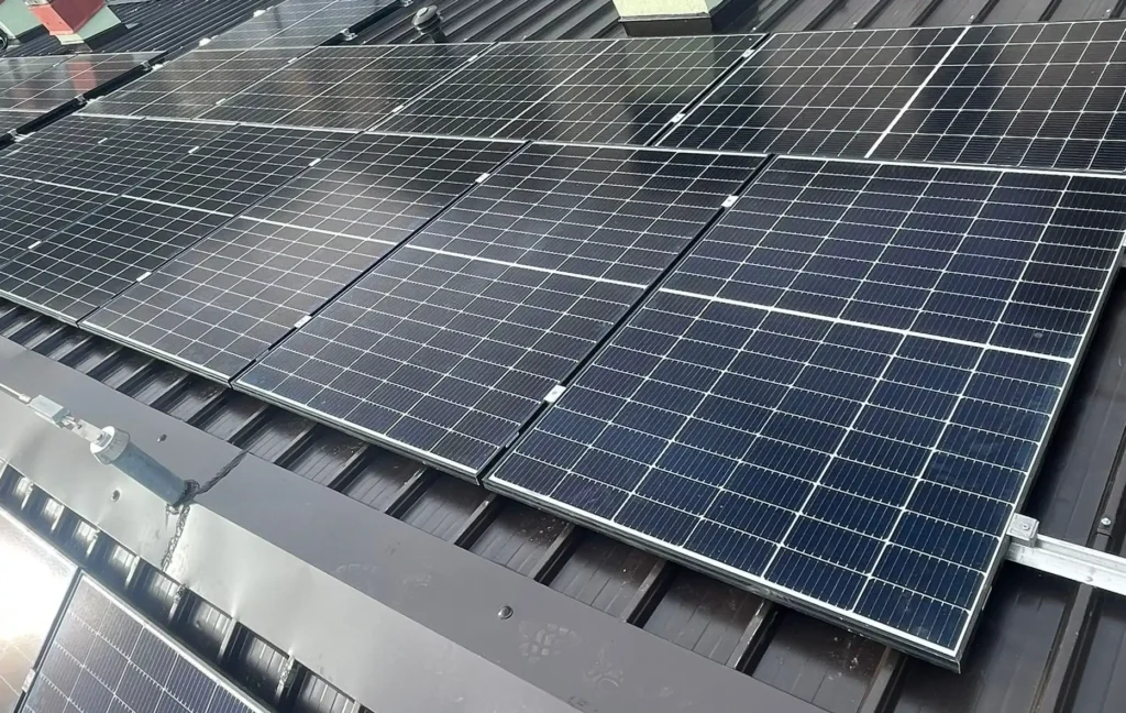 Dettaglio ravvicinato di pannelli solari fotovoltaici neri installati su un tetto scuro a falda, con i supporti di montaggio visibili.